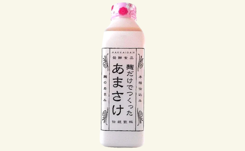 温かい湯気が立ち上るマグカップに注がれた甘酒。背景には他社製品と比較するように、パッケージの異なる甘酒が並ぶ。八海山のパッケージが際立って見える。